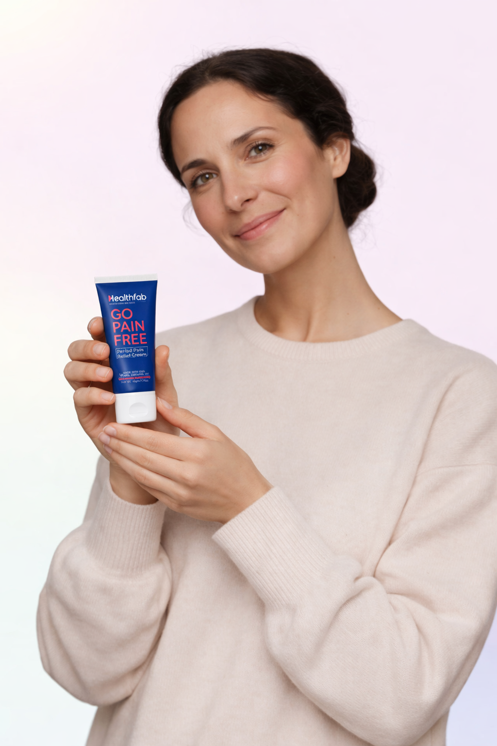 Woman holding a tube of 'Go Pain Free' cream against a plain background